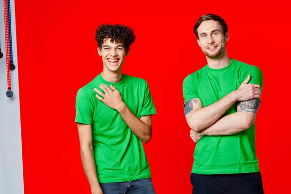 Zwei Männer in grünen T-Shirts stehen neben freundschaftsrotem Hintergrund — Stockfoto