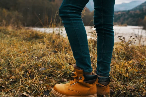 Pernas femininas em botas e jeans na natureza no outono nas montanhas — Fotografia de Stock
