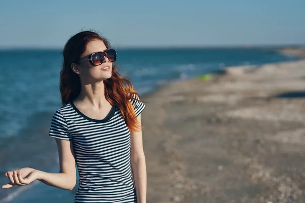 Kobieta spacerująca po plaży w lecie w okularach i koszulce w paski — Zdjęcie stockowe