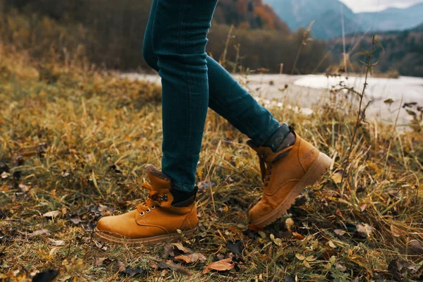 Pernas femininas em botas e jeans na natureza no outono nas montanhas — Fotografia de Stock