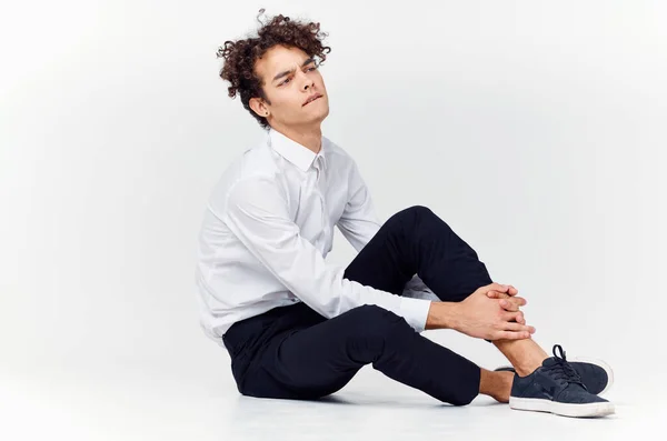 A teenager in a suit and sneakers sits on the floor In a bright room side view — Stock Photo, Image