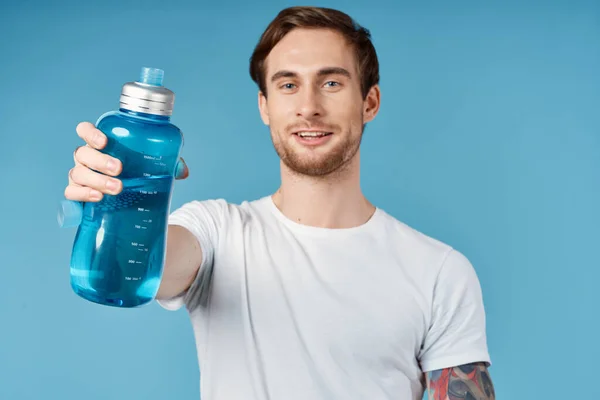 Uomo sportivo in t-shirt bianca con bottiglia d'acqua blu davanti a lui studio — Foto Stock