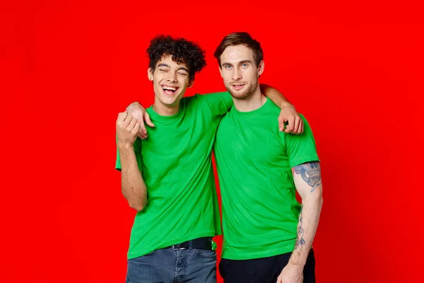 Zwei Männer grüne T-Shirts umarmen Emotionen Freundschaft roter Hintergrund — Stockfoto