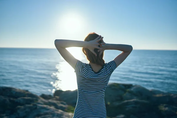 Felice viaggiatore donna gesticolando con le mani vicino al mare nella natura e al tramonto in lontananza — Foto Stock