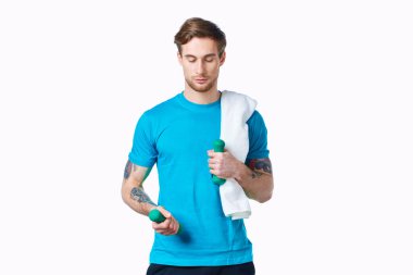 Elinde dambıllar, omuzlarında havluyla egzersiz yapan sportif bir adam.