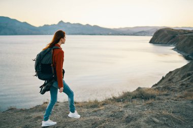 Kadın deniz kenarındaki dağlarda dinleniyor ve sırt çantasıyla turizm modeline biniyor.