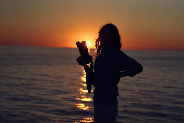 Woman at sunset near the sea with a camera in hand — Stock Photo, Image