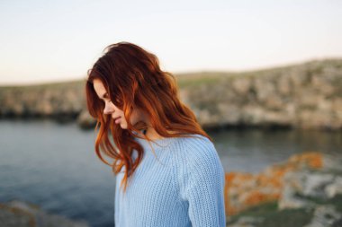 Açık havada kazak giyen kızıl saçlı kadın kayalık dağlarda tatil yapıyor.