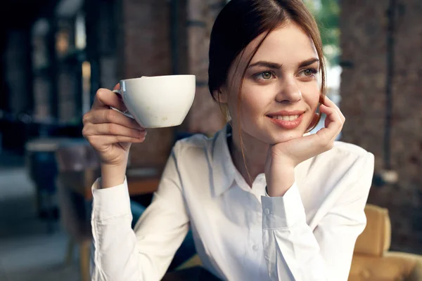 Mulher de negócios bonita na camisa branca senta-se em um café com uma xícara de café — Fotografia de Stock