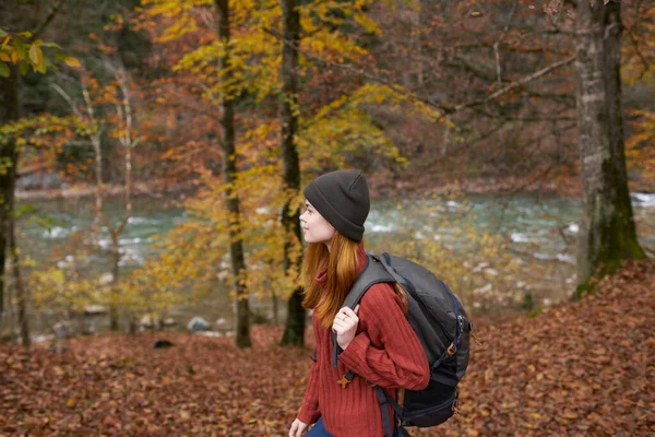 Vue latérale de la femme heureuse dans le parc en automne près de la rivière et sac à dos sur son dos — Photo
