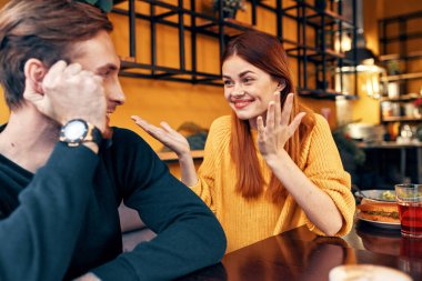 Bir kadın elleriyle hareket eder ve elinde saati olan yakışıklı bir adama bir şeyler söyler.