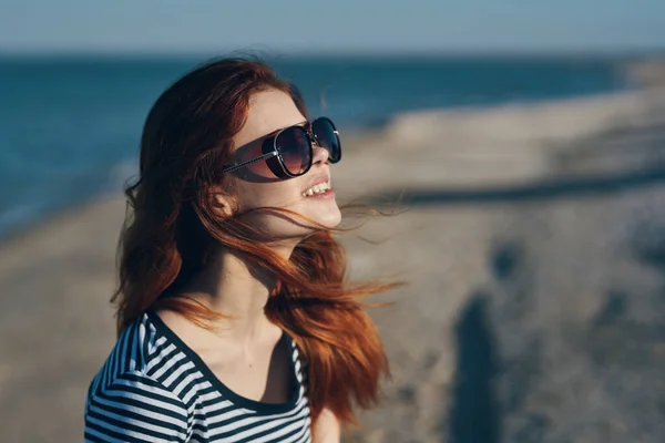 Mulher em óculos e em uma camiseta listrada ao pôr do sol ou lá perto da vista para o mar a partir da varanda — Fotografia de Stock