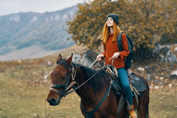 Mulher caminhante com uma mochila monta um cavalo nas montanhas natureza viagens — Fotografia de Stock