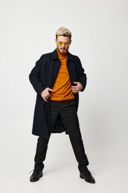 Koyu renk elbiseli, turuncu kazaklı ve pantolon giyen şık bir adam.