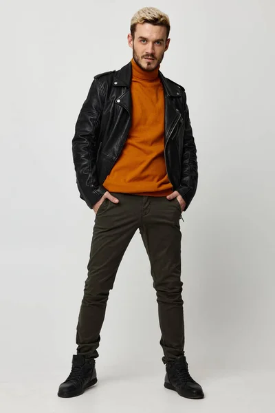 Man in een oranje trui houdt zijn handen in zijn broek zakken zwart schoenen lederen jas mode stijl — Stockfoto