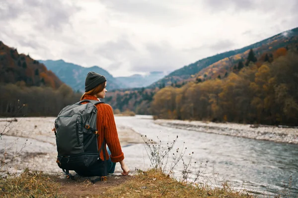 Un voyageur dans une veste avec un sac à dos sur son dos chapeau montagnes paysage rivière — Photo