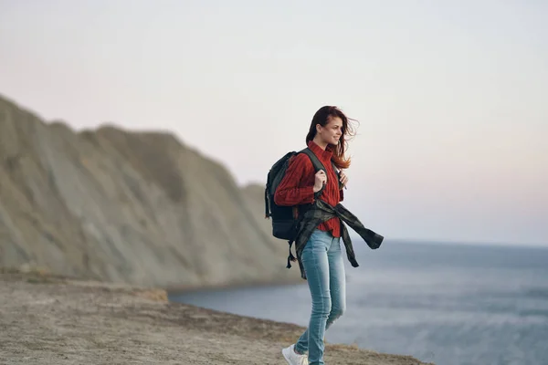 Woman hiker travels in the mountains in nature with a backpack on her back red sweater rock — Stock Photo, Image