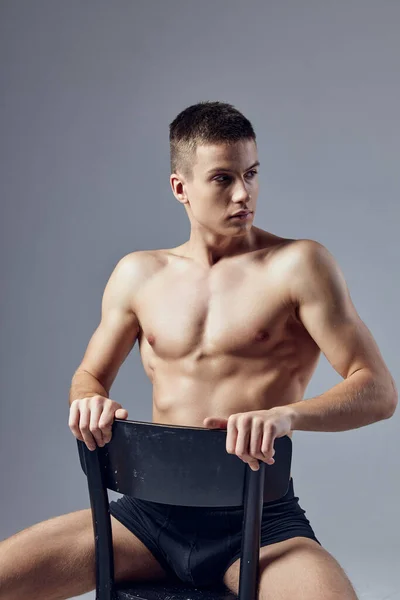 Ragazzo sexy con muscoli muscolosi seduto su una sedia vista ritagliata — Foto Stock