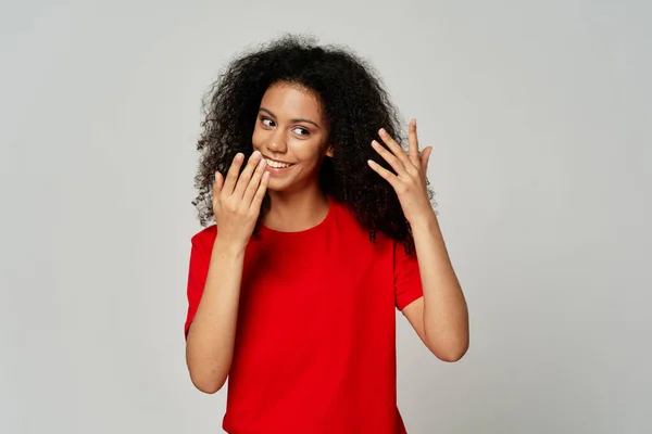 Vrolijke vrouw met krullend haar rood t-shirt gebaren met handen emoties geïsoleerde achtergrond — Stockfoto