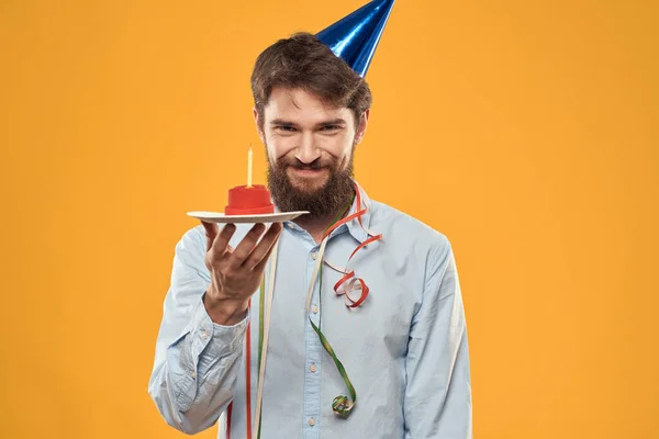 Homme joyeux avec un gâteau sur un fond jaune casquette de vacances d'anniversaire sur sa tête — Photo