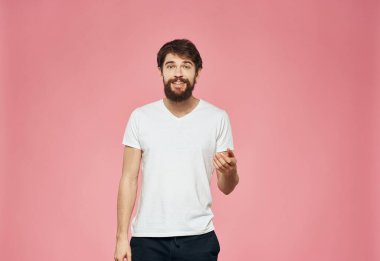 Pembe arka planda tişörtlü ve pantolonlu sakallı adam.