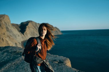 Sırtında sırt çantasıyla deniz kenarında kazaklı bir kadın.