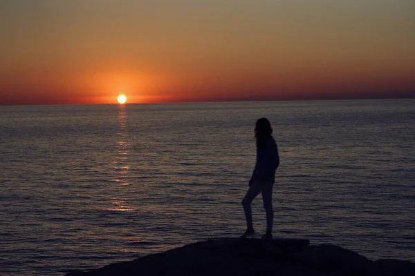 Puesta de sol en las montañas junto al mar y una silueta femenina en la playa — Foto de Stock