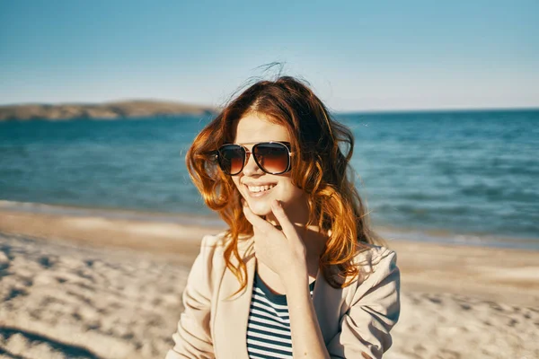 Kobieta z okularami czerwony włosy model beżowy kurtka piasek plaża morze — Zdjęcie stockowe