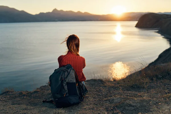 Un viaggiatore in maglione si siede sulla riva del mare e guarda il tramonto — Foto Stock