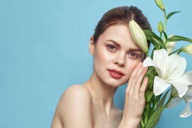 Mavi arka planda bir buket beyaz çiçekli güzel bir kız çıplak omuz portresi.