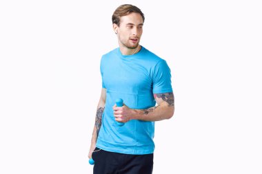 Bir adam elinde dambıllarla spor salonuna gider. Hafif bir arka plan ve dövme modeli.