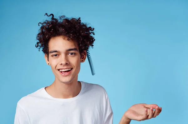 Riccio ragazzo in un bianco t-shirt pettine emozioni blu sfondo — Foto Stock