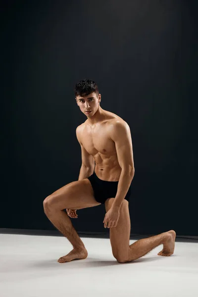 Человек в темных трусиках с обнаженным мускулистым телом стоит на коленях — стоковое фото