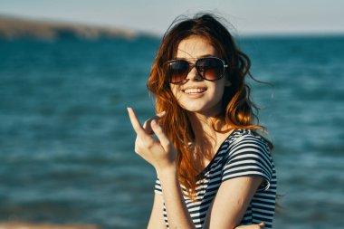 Deniz kenarındaki dağlarda güneş gözlüklü kızıl saçlı bir kadının portresi ve kahkahalar atan turizm.