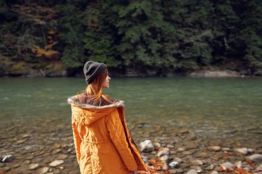 Nehir kıyısındaki sonbahar ormanında yürüyen bir kadın.