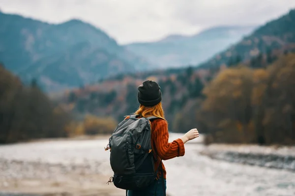 Femme sur la rive de la rivière avec sac à dos Voyage randonnée montagnes au loin — Photo