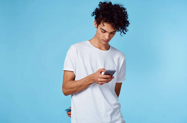 Man in wit t-shirt krullend haar telefoon in handen technologie blauwe achtergrond — Stockfoto