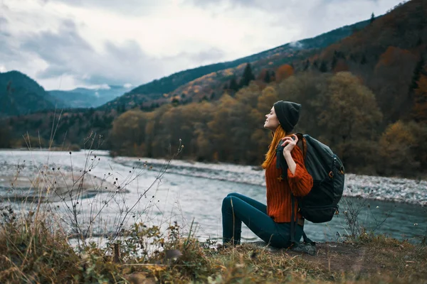 Жінка біля річки в горах з рюкзаком на плечах відпочиває в осінньому лісі — стокове фото
