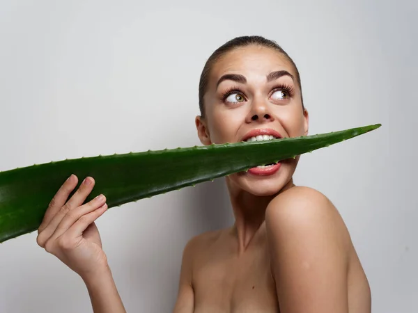 Grünes Aloe-Blatt im Frauenmund mit überraschendem Blick und nackten Schultern — Stockfoto