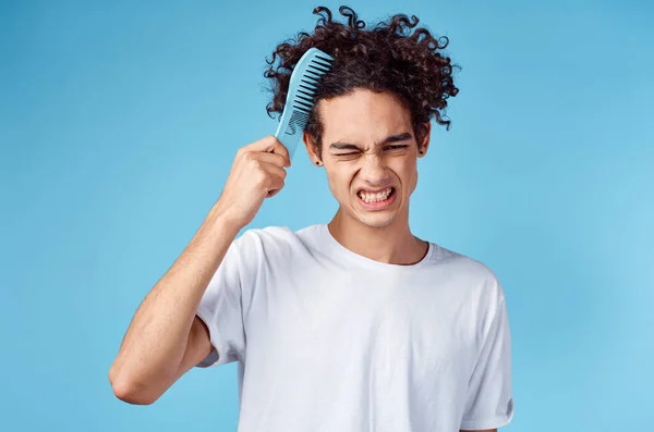 Негодующий парень расчесывает волосы синей расчёской на изолированном фоне обрезанного вида — стоковое фото