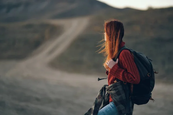 woman tourist with a backpack on his back resting in the mountains and the road in the distance