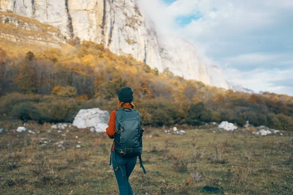 Un viajero en pantalones vaqueros suéter con una mochila en la espalda y un cálido sombrero montañas paisaje otoñal — Foto de Stock