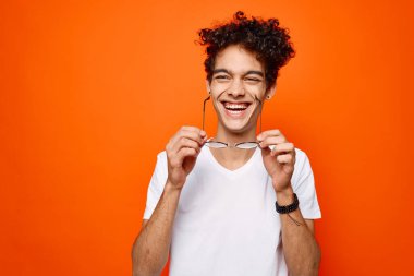 Neşeli adam kıvırcık saçlı gözlüklü, moda turuncu arka planlı.