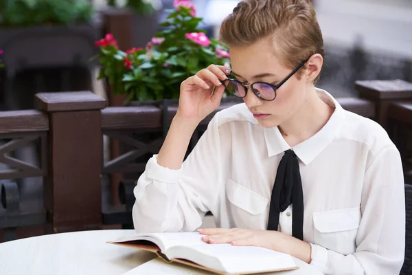 Vrouw in shirt en das aan de tafel boek onderwijs interieur bloemen — Stockfoto