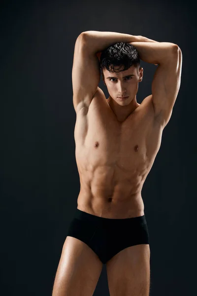 Sportos férfi felpumpált izmos test tartja a kezét a feje fölött pózol macho sötét háttér — Stock Fotó