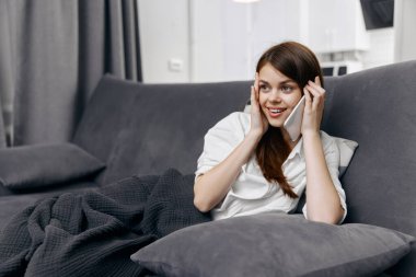 Odadaki kanepede telefonda konuşan mutlu bir kadın ve bacaklarında bir ekose.
