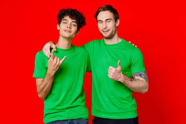 Due uomini che si abbracciano in magliette verdi su sfondo rosso — Foto Stock