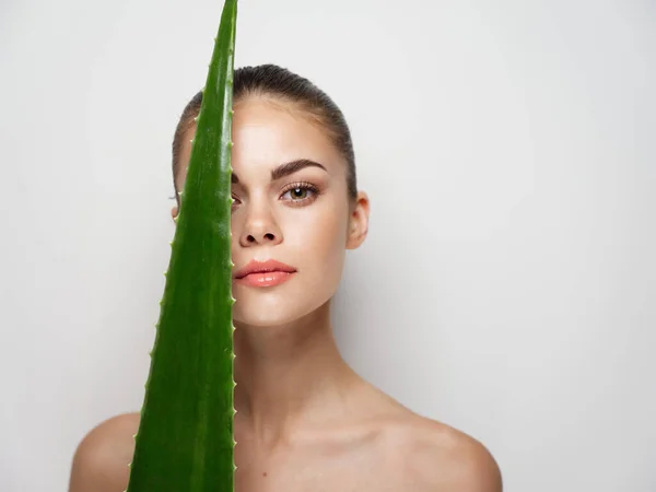 Mulher toca rosto com folha de aloés no fundo de luz close-up retrato — Fotografia de Stock