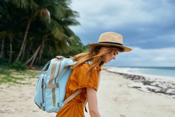 Mulher viaja na praia perto do mar com uma mochila nas costas e árvores altas no fundo — Fotografia de Stock