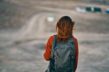 Sırt çantalı bir kadın, dağlarda doğada dinleniyor. Arka plandaki kumdan binalar, turizm...